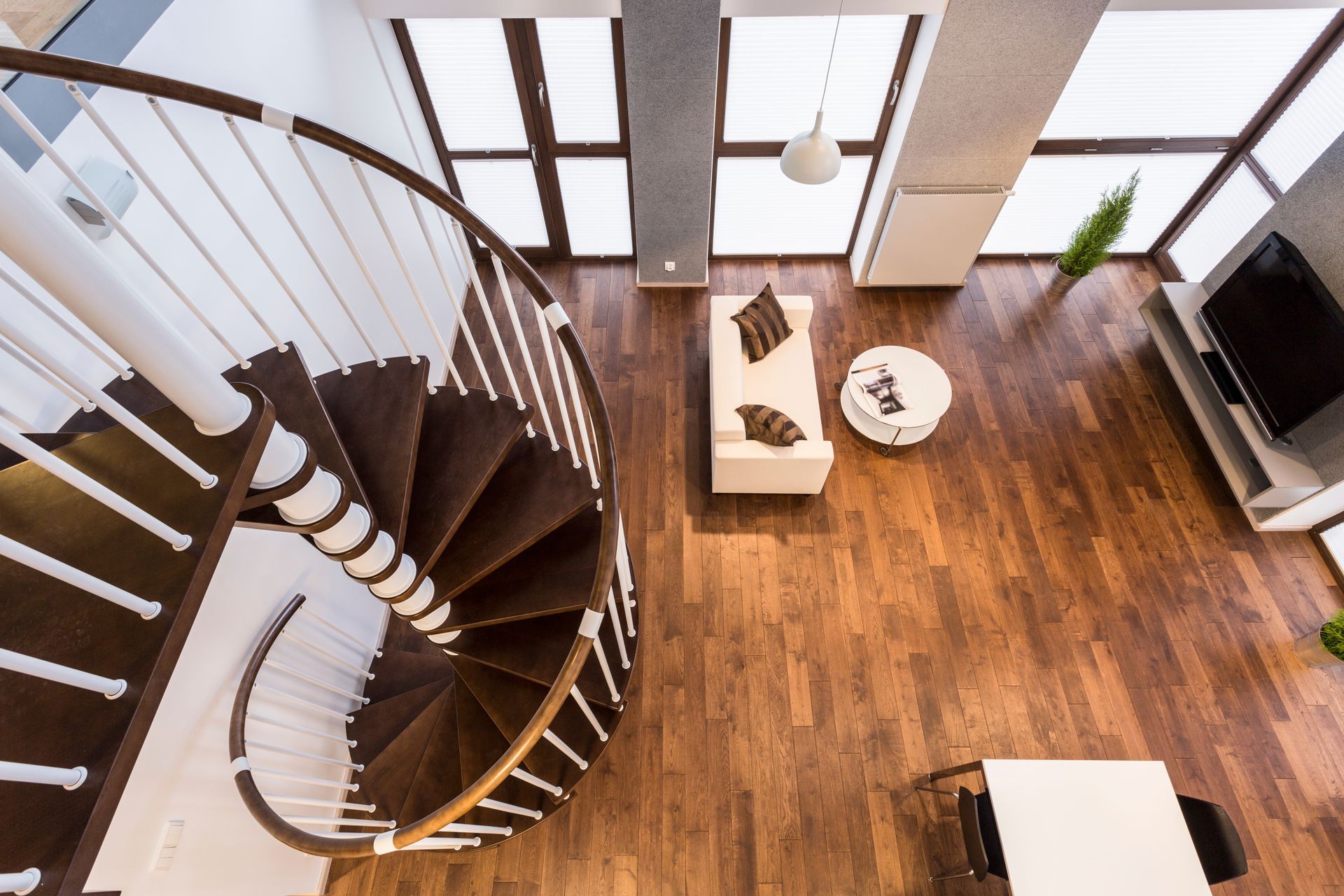 Vista en ángulo alto de una sala de estar moderna con una escalera de caracol, pisos de madera y muebles blancos.