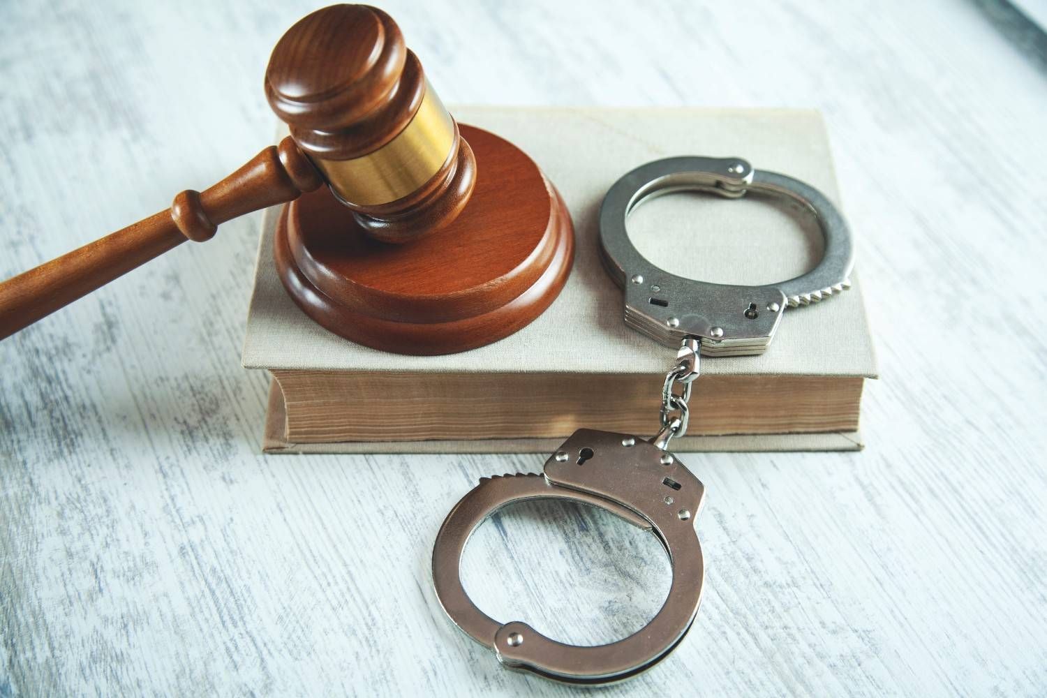 Mazo de juez junto a unas esposas abiertas sobre un libro, símbolo de la ley y la justicia penal.
