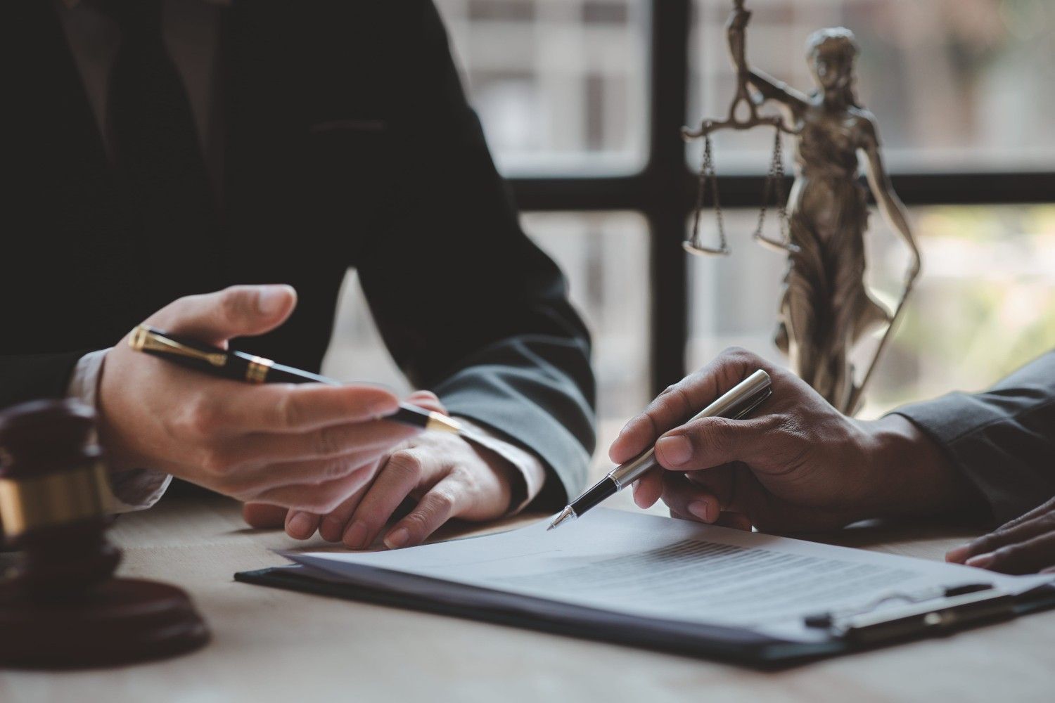 Dos personas revisan un documento en un escritorio con un bolígrafo y una pequeña estatua al fondo.
