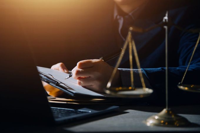 Un abogado tomando notas junto a una balanza de latón en una oficina con poca luz.