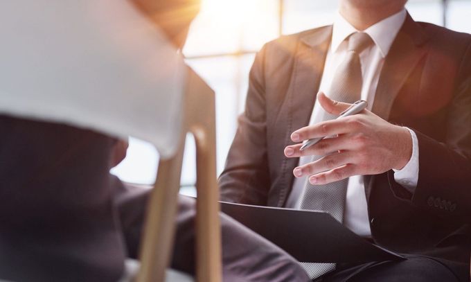 Empresario con traje sosteniendo un bolígrafo durante una reunión, con un ordenador portátil en primer plano.