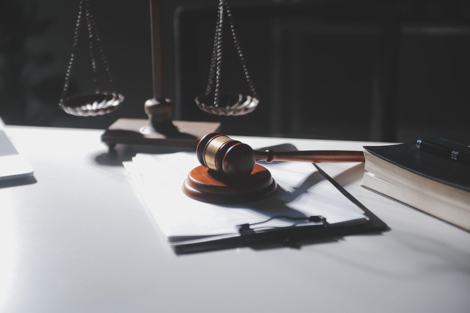 Un mazo de juez sobre un escritorio con una balanza de la justicia y un libro de leyes al fondo.