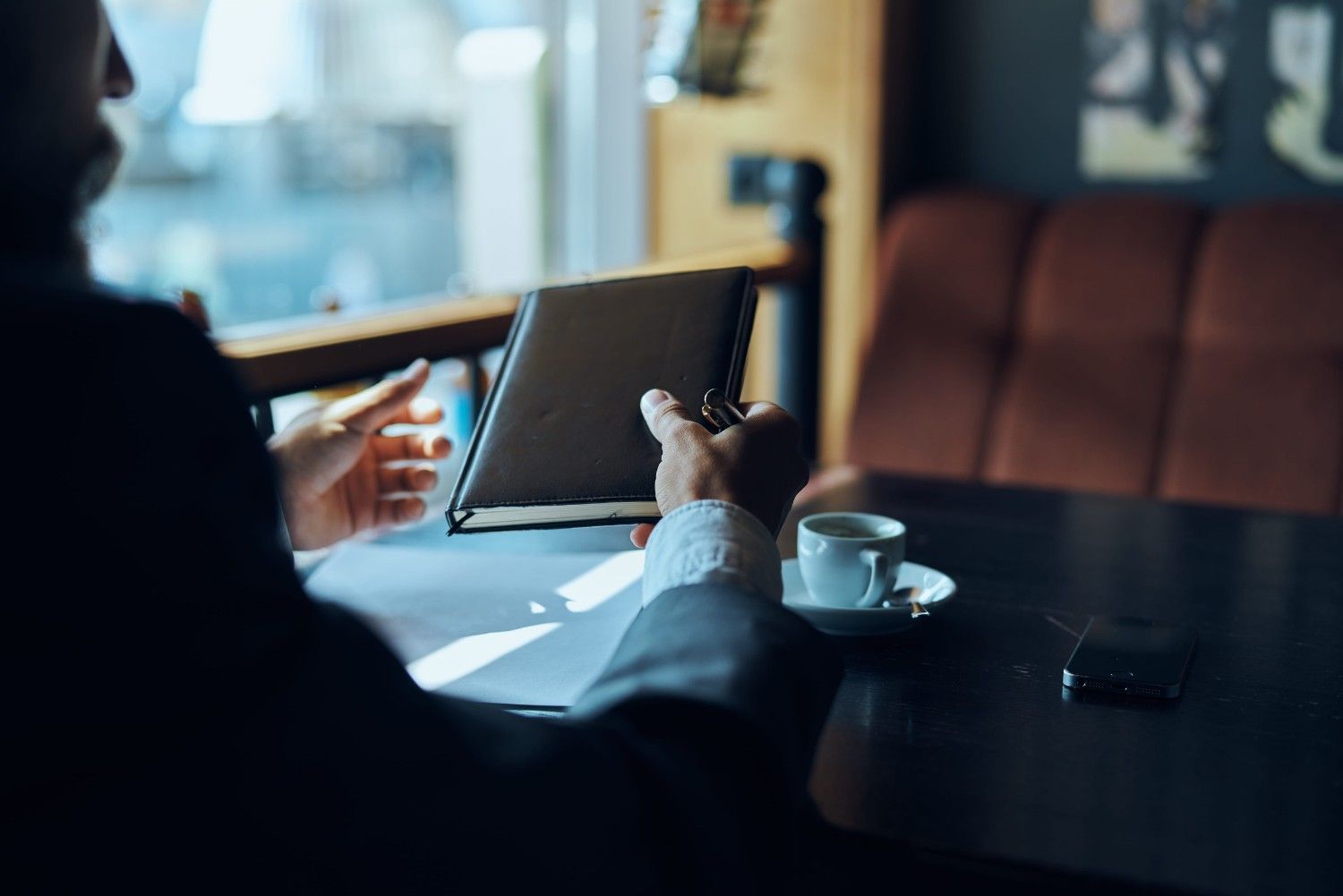 Una persona sostiene una tableta en la mesa de una cafetería con una taza de café y un teléfono cerca.