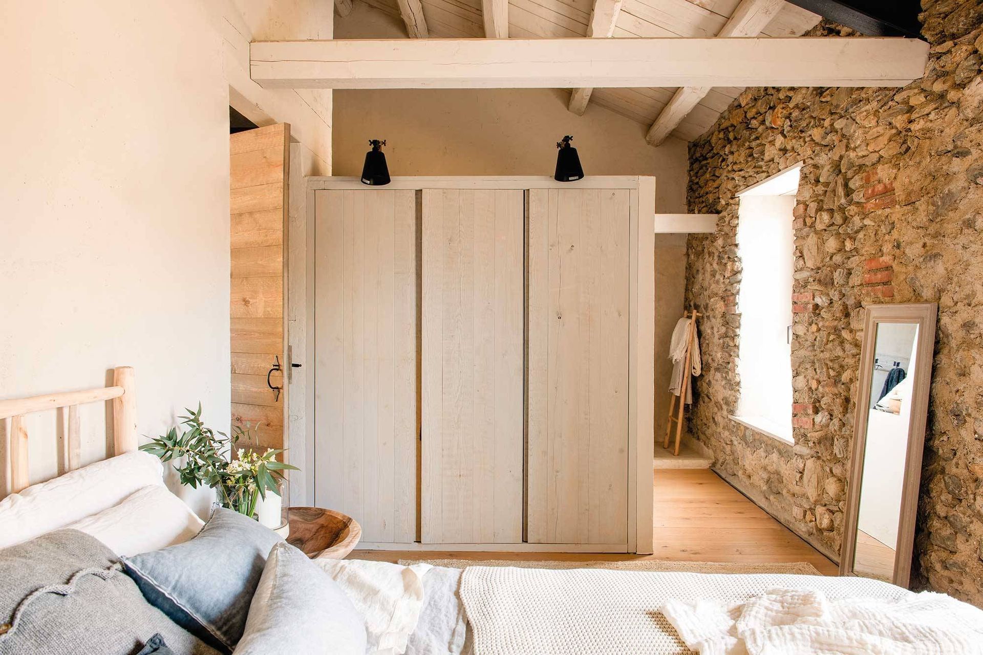 Dormitorio con cama de madera y armario; pared de piedra y espejo.