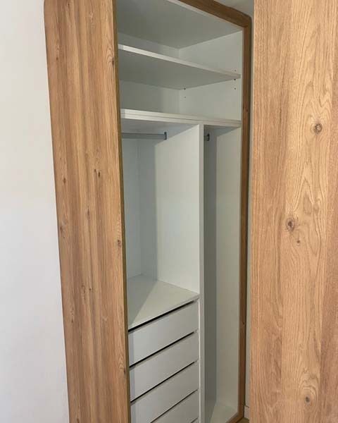 Un armario con puerta de madera y estantes y cajones blancos.