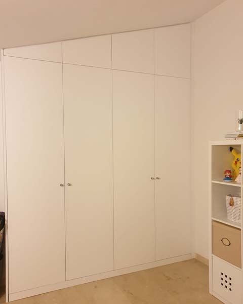 Un dormitorio con muchos armarios blancos y un estante.