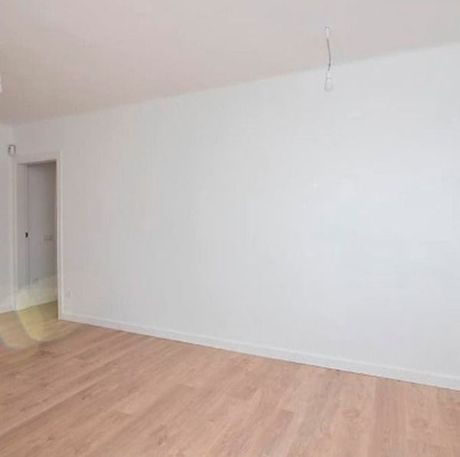 Una sala de estar vacía con pisos de madera y paredes blancas.