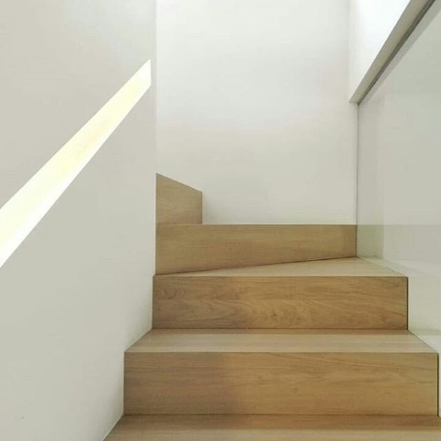 Una escalera de madera con una pared blanca y una barandilla de cristal.
