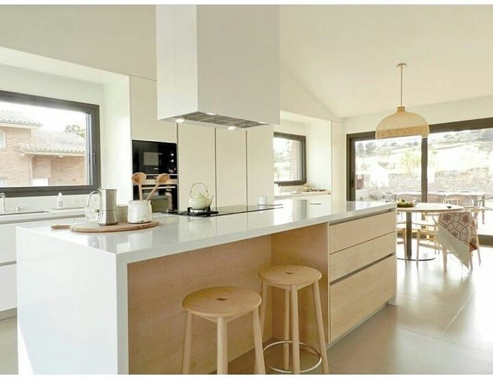 Una cocina con gabinetes blancos y taburetes de madera y una gran isla.