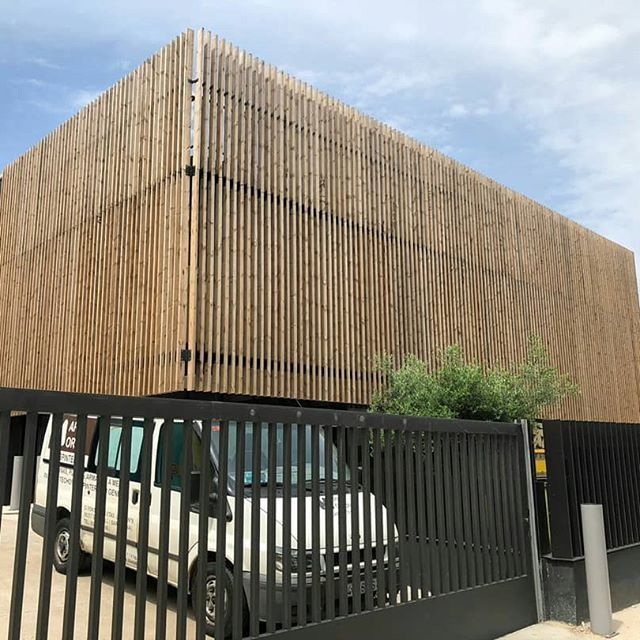 Una furgoneta blanca está estacionada delante de un edificio con fachada de madera detrás de una valla.