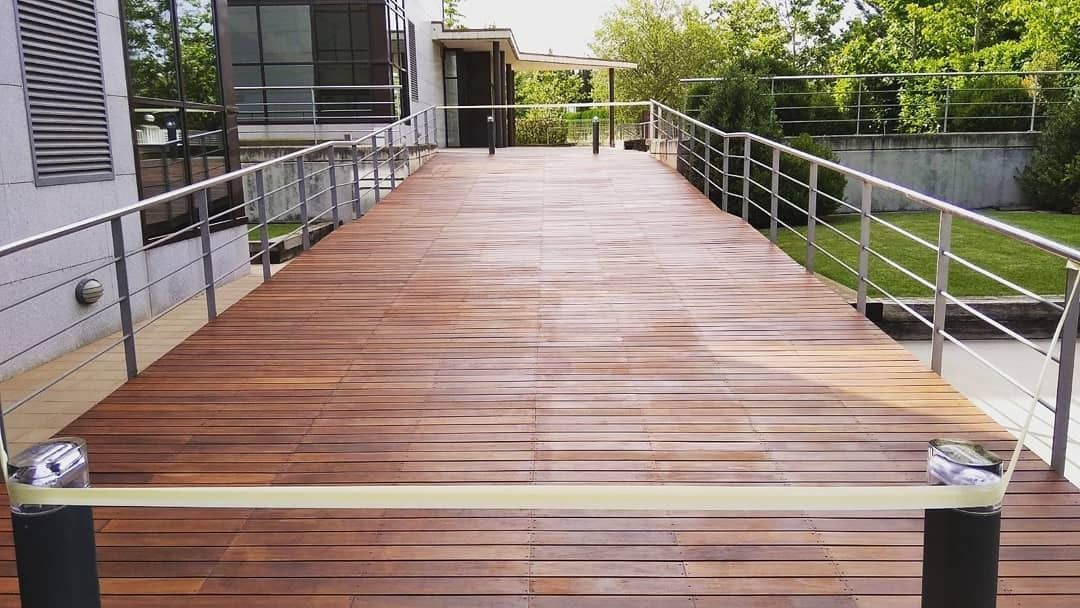 Una terraza de madera con barandilla de acero inoxidable que conduce a una casa.