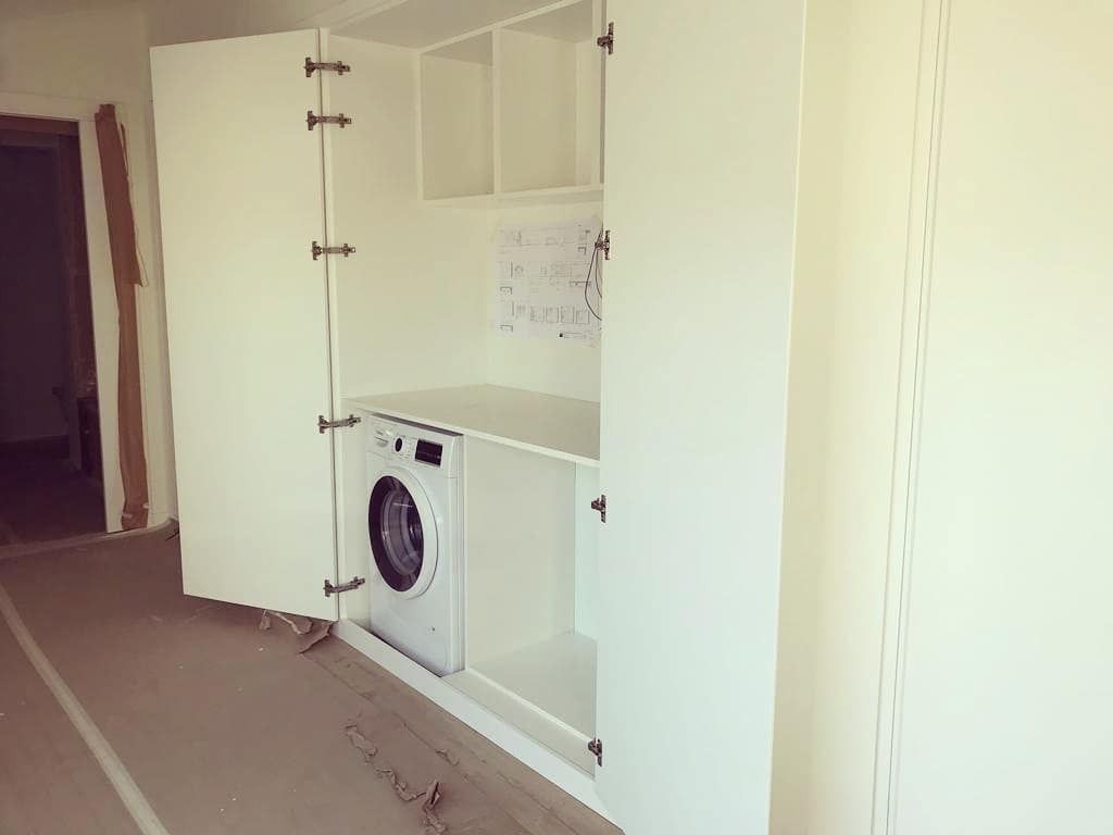 Una lavadora está dentro de un mueble blanco.