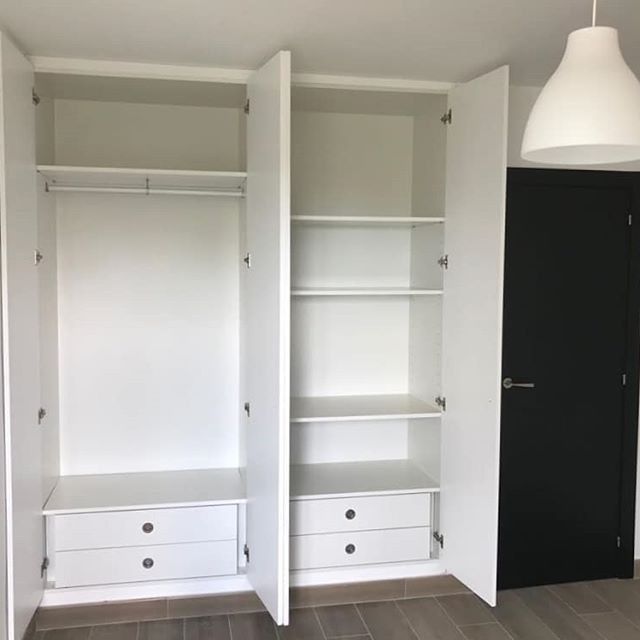 Un armario blanco con cajones y estantes en una habitación con una puerta negra.