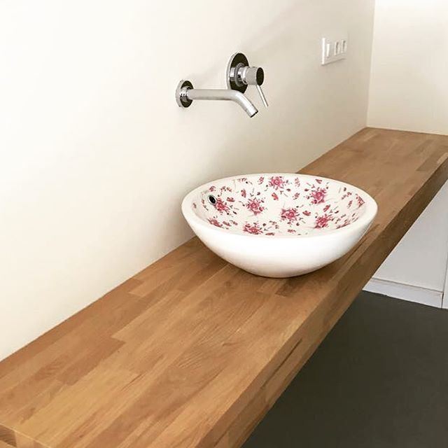 Un lavabo de baño con un diseño floral se encuentra sobre una encimera de madera.