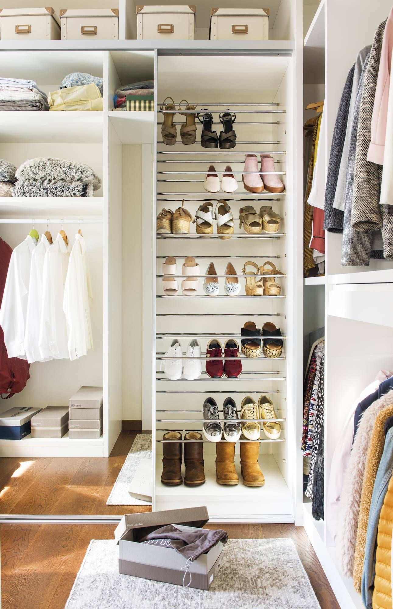 Armario blanco organizado con zapatero. Suelo de madera marrón, ropa colgada. Cajas en los estantes superiores.