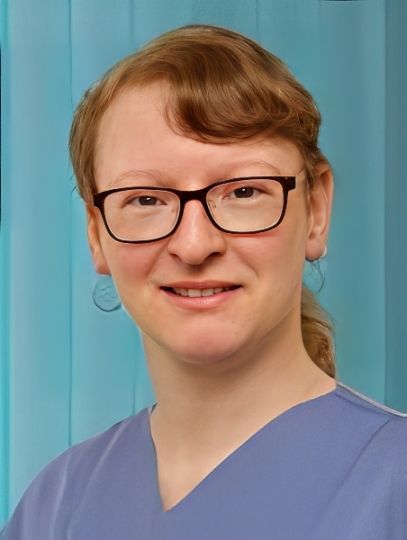 Frau mit Brille und kastanienbraunem Haar lächelt in einem blauen OP-Oberteil.