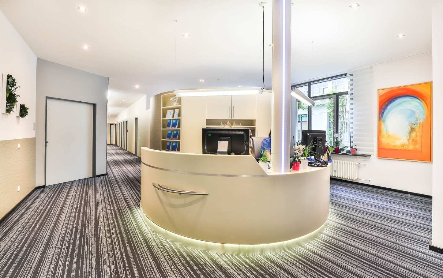 Moderner Empfangsbereich einer Arztpraxis mit geschwungenem Schreibtisch, Kunstwerken und langem Flur.