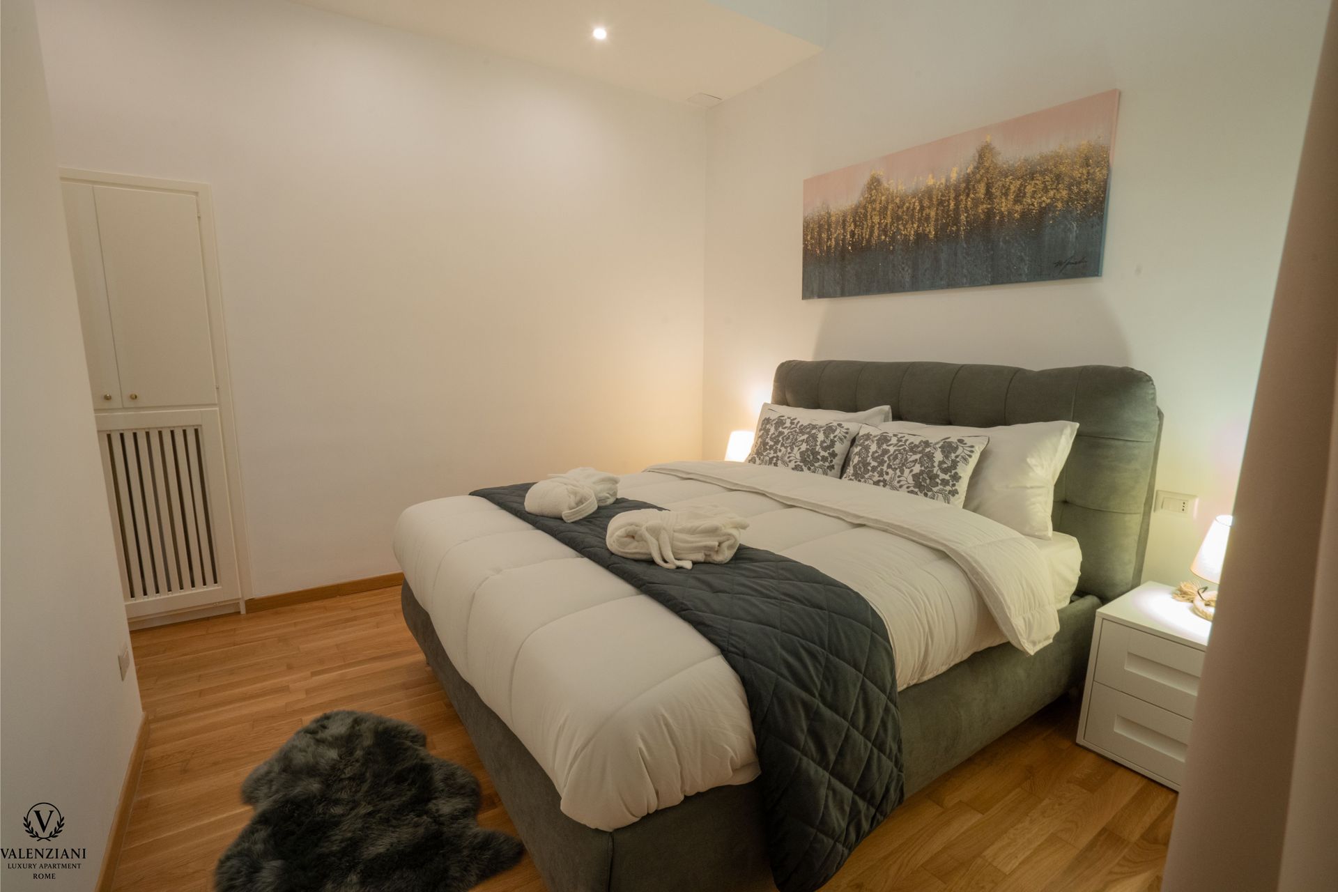 Bedroom with bed, white bedding, art, and wooden floor.
