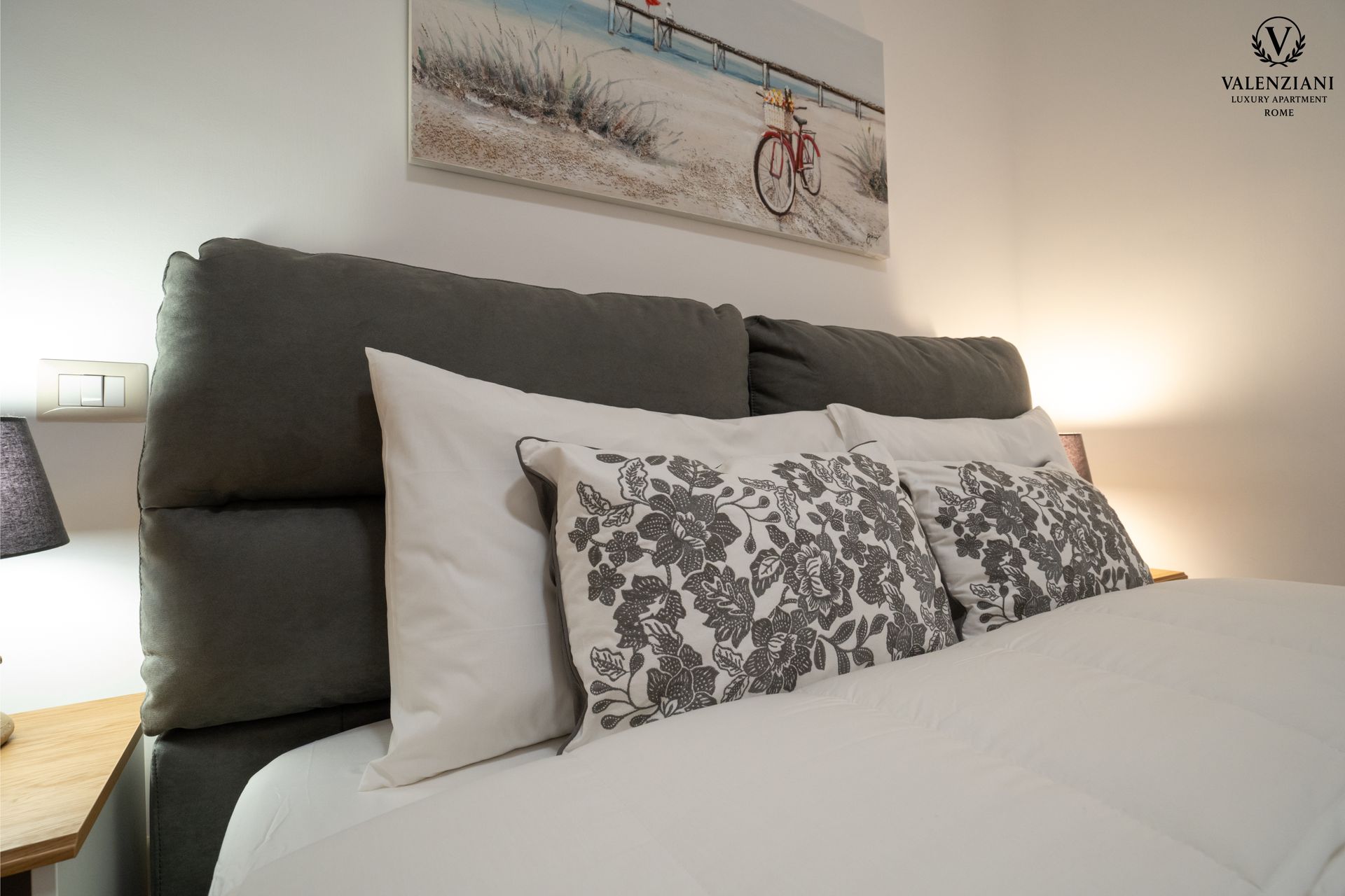Bedroom with a gray headboard, white bedding, decorative pillows, and a beach scene painting.