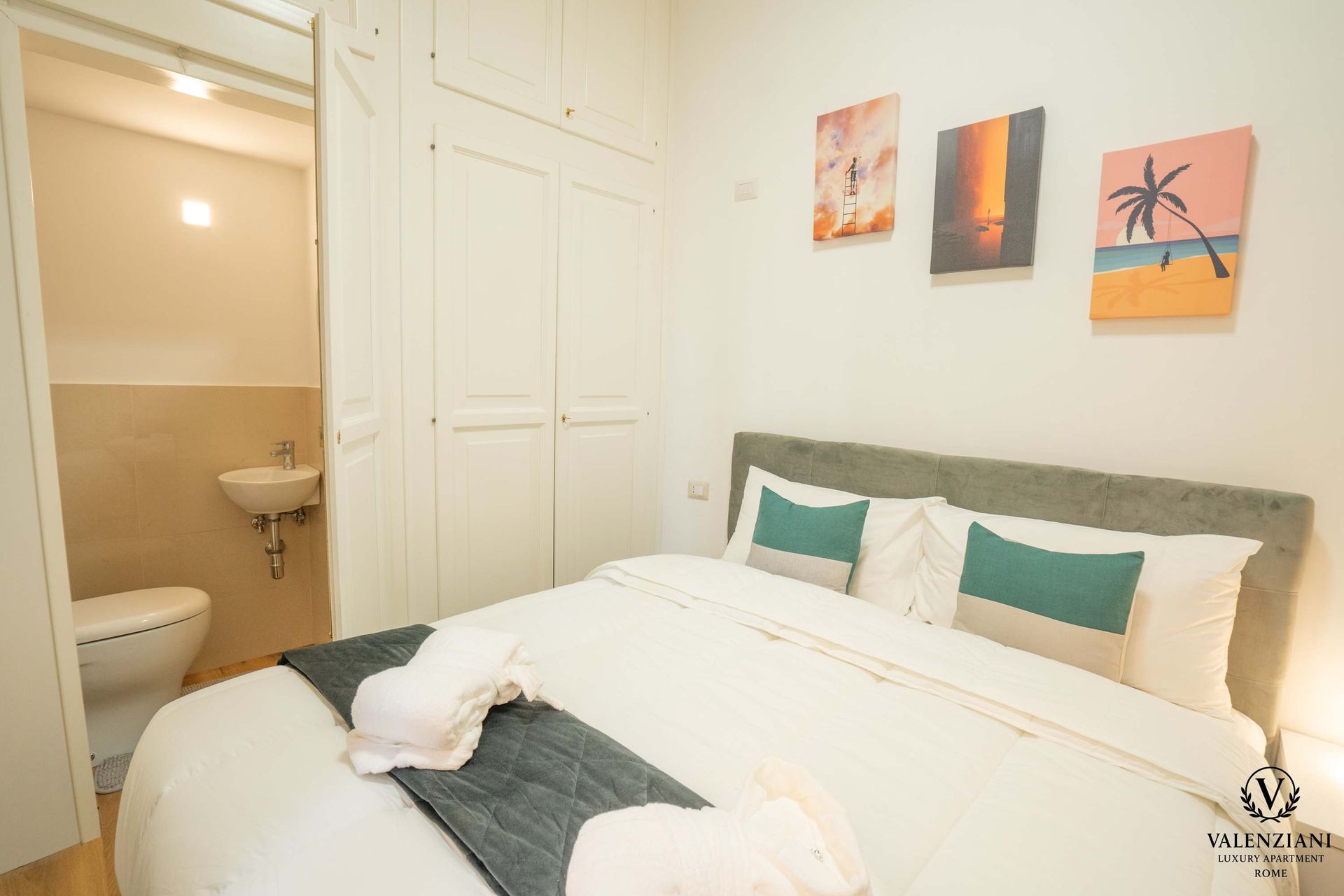 Bedroom with a bed, closet, and a small bathroom. Tropical artwork hangs above the bed.