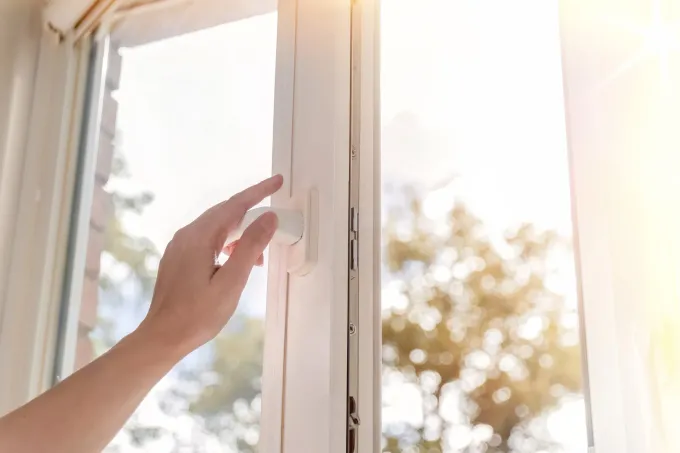 Mano abriendo una ventana blanca, la luz del sol entra desde afuera.