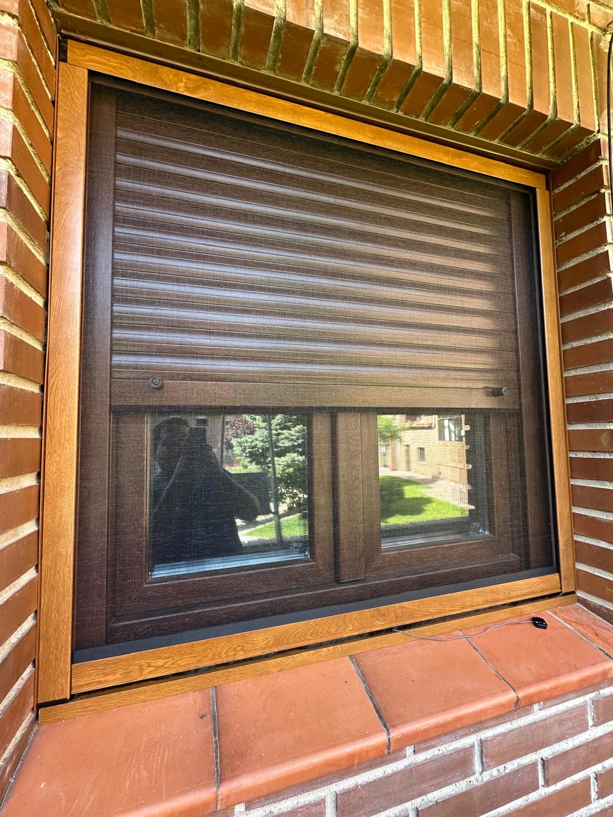 Ventana con contraventanas marrones y marco en un edificio de ladrillo; parcialmente abierta, mostrando una vista.