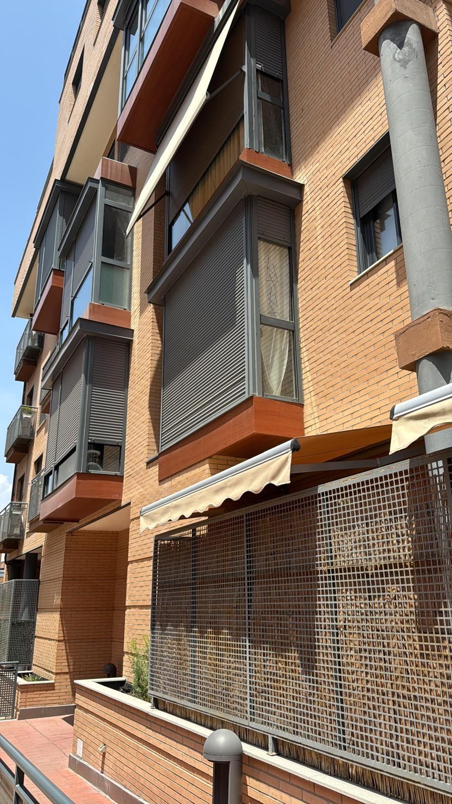 Edificio de ladrillo con balcones y toldos bajo un cielo azul.