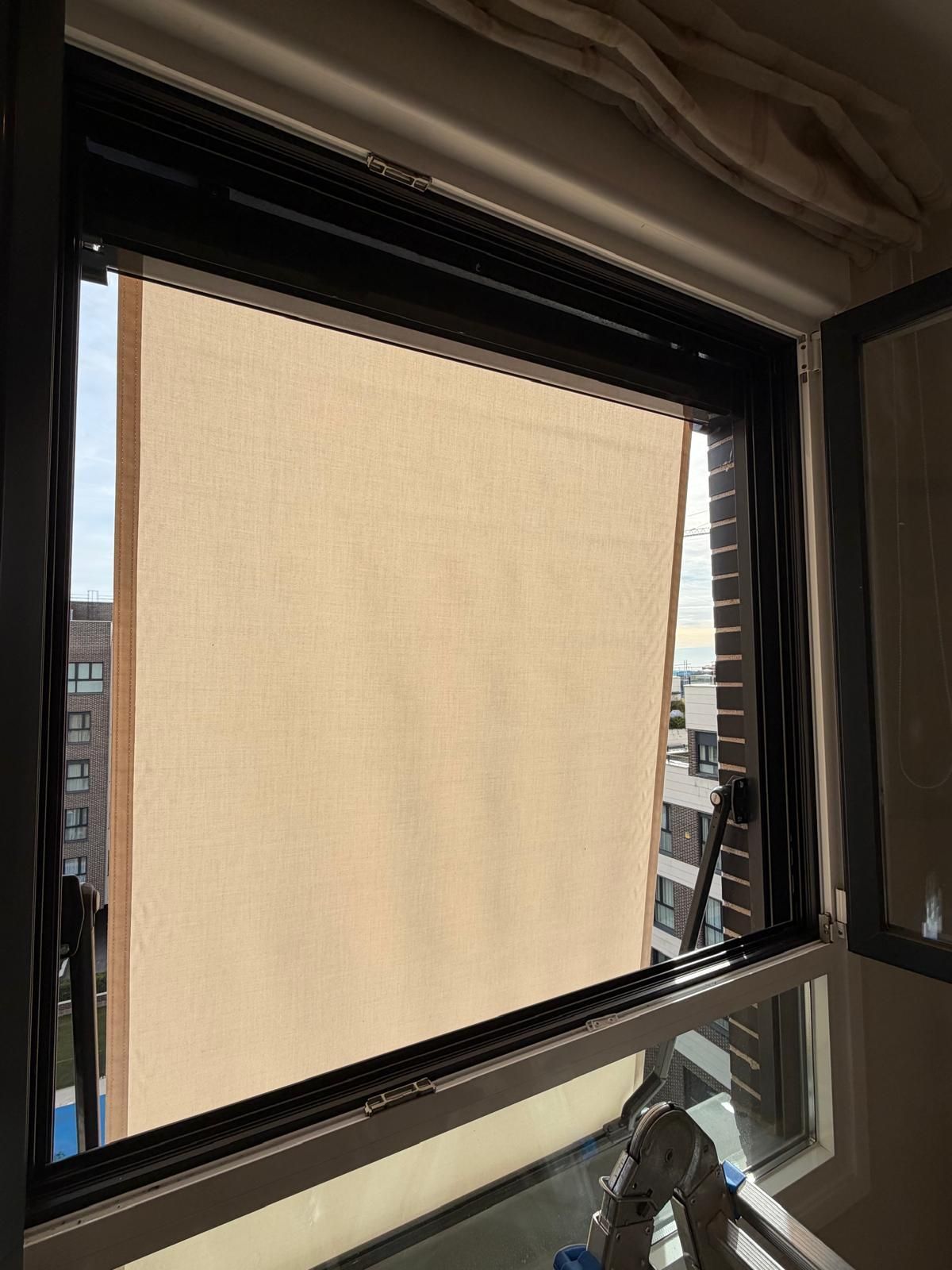 Ventana abierta con persiana color canela. Vista de edificios visibles a través de la ventana.