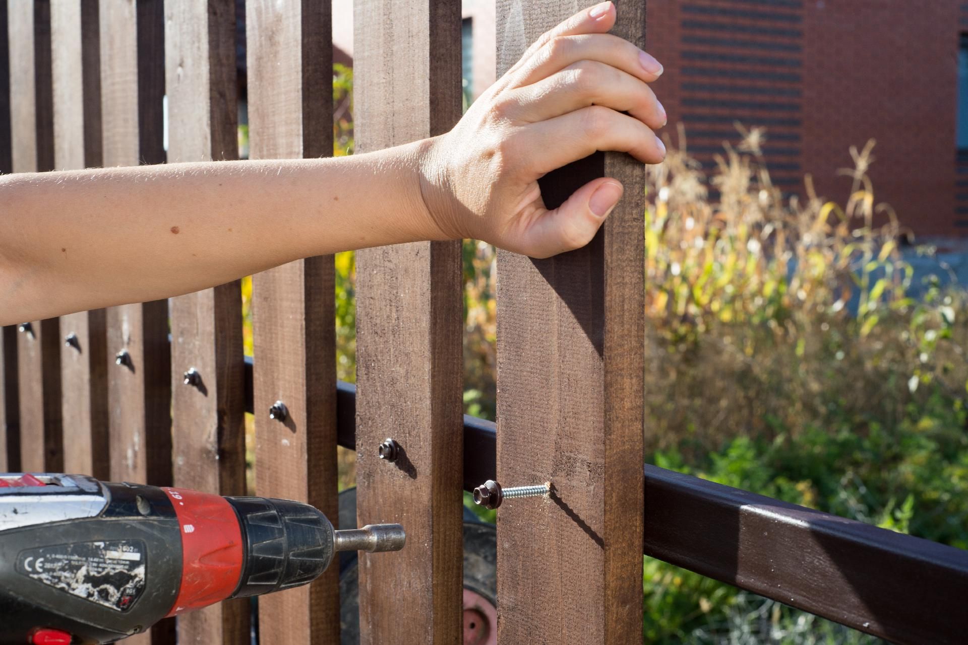Hand streicht Holzzaun im Garten mit Pinsel