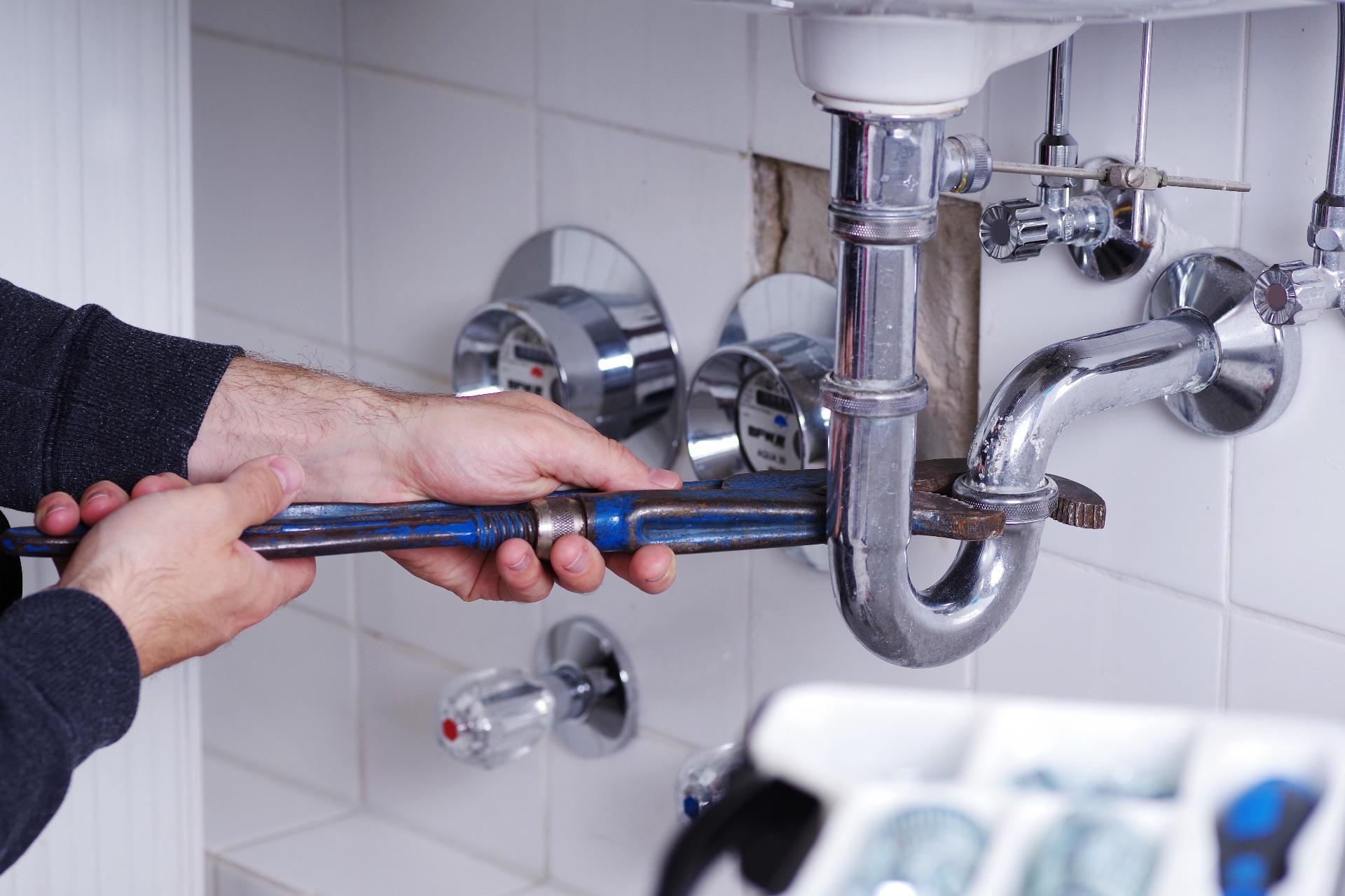 Hand arbeitet an Rohrleitungen unter Waschbecken, Sanitärreparatur