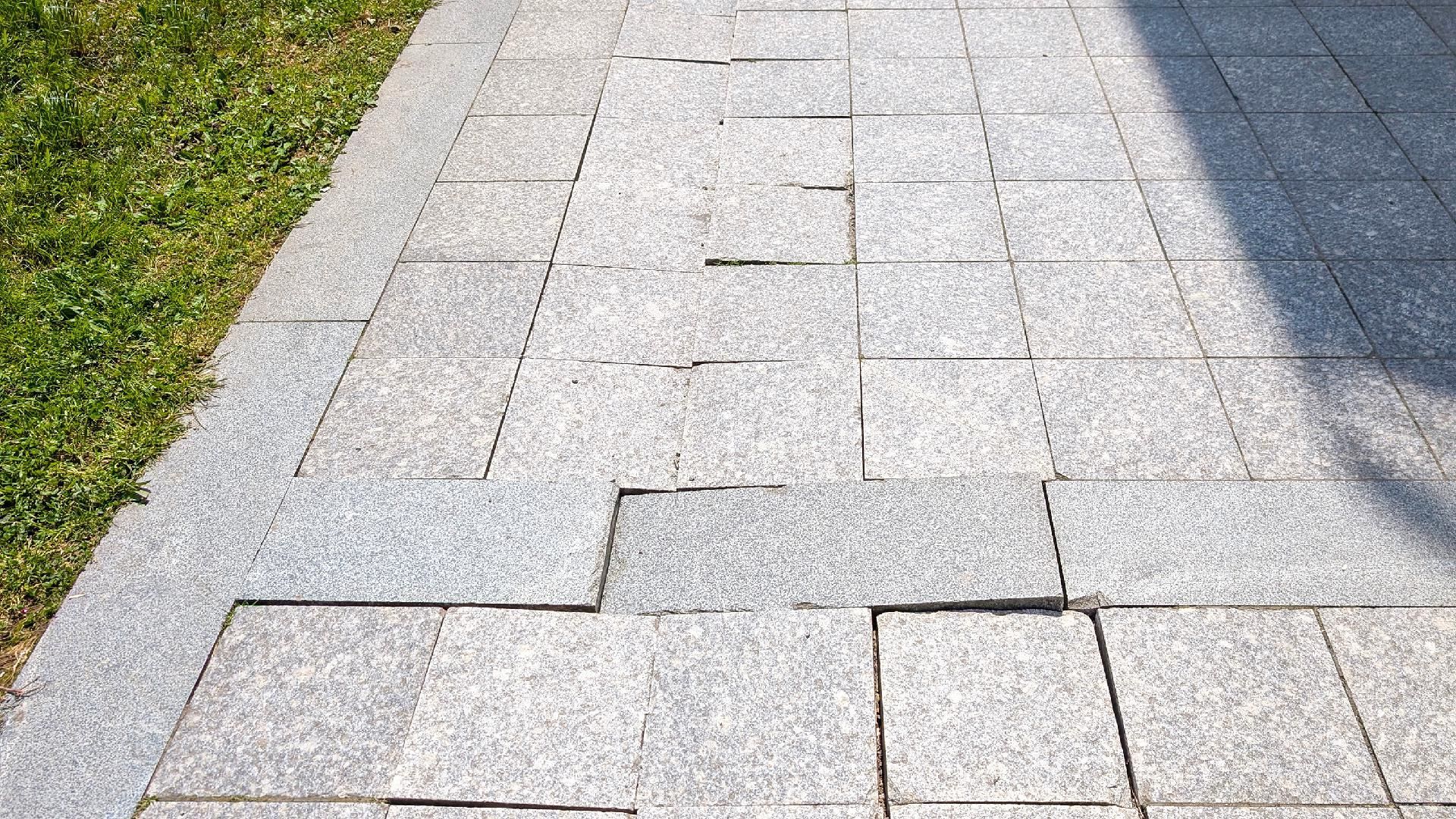 Gehweg mit beschädigten Pflastersteinen, unebene Fläche im Außenbereich