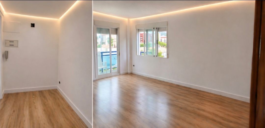Sala de estar moderna y vacía con suelos de madera, paredes blancas, iluminación empotrada, grandes ventanales y puerta que da al balcón.