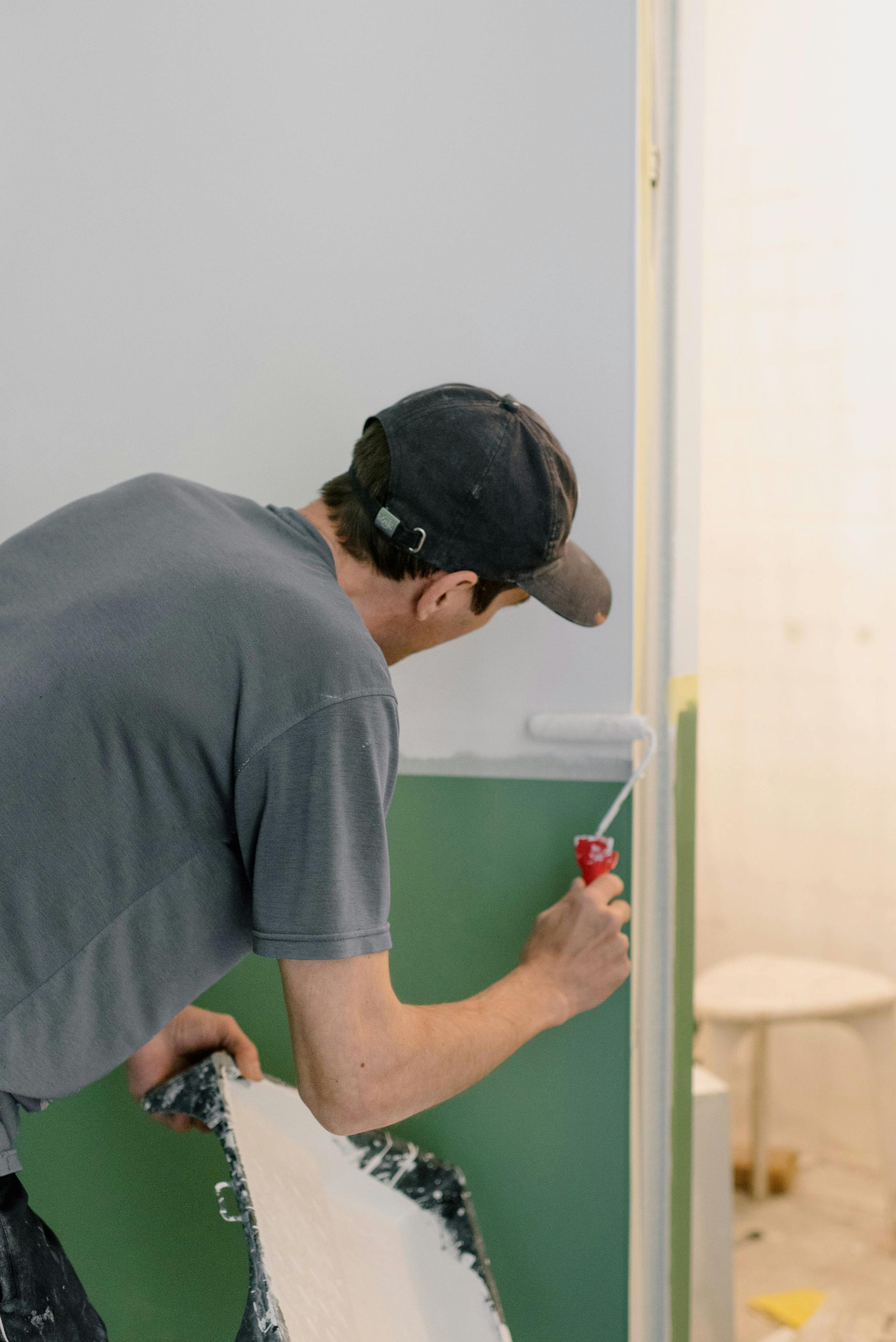 Persona instalando paneles de yeso con un panel verde y una herramienta roja en una habitación interior.