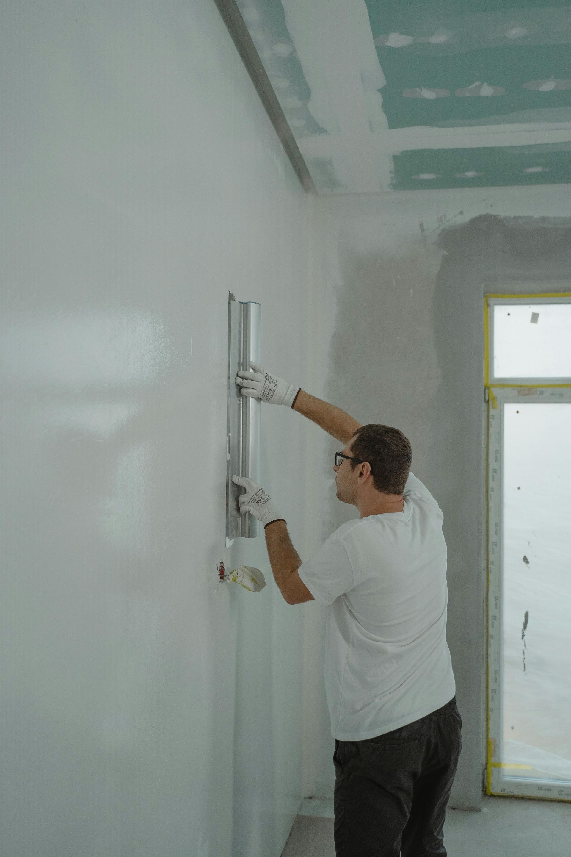 Obrero aplicando yeso a una pared blanca en una habitación en construcción.