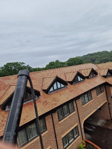 Tilted view of a brick building with red roof and dormer windows under a cloudy sky
