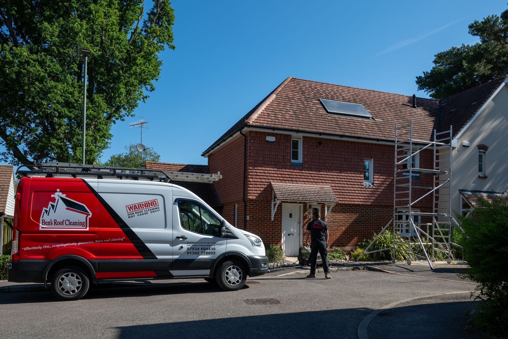 Red and white moving van parked by a brick house, with a person standing in the driveway