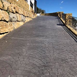 Un camino de entrada de hormigón con un muro de piedra al costado.