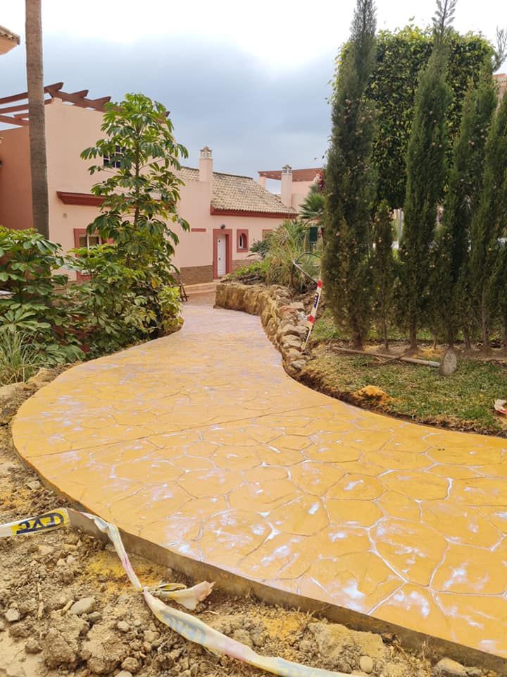 Una pasarela de hormigón en un jardín con una casa al fondo.