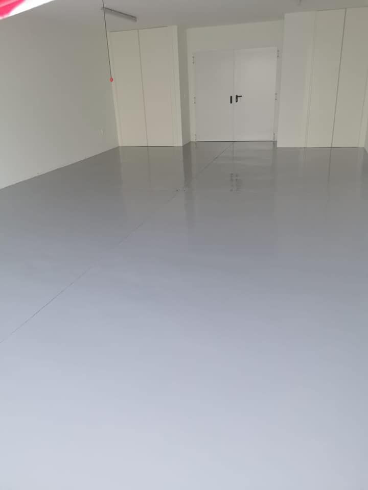 Una gran habitación vacía con suelo gris y paredes blancas.