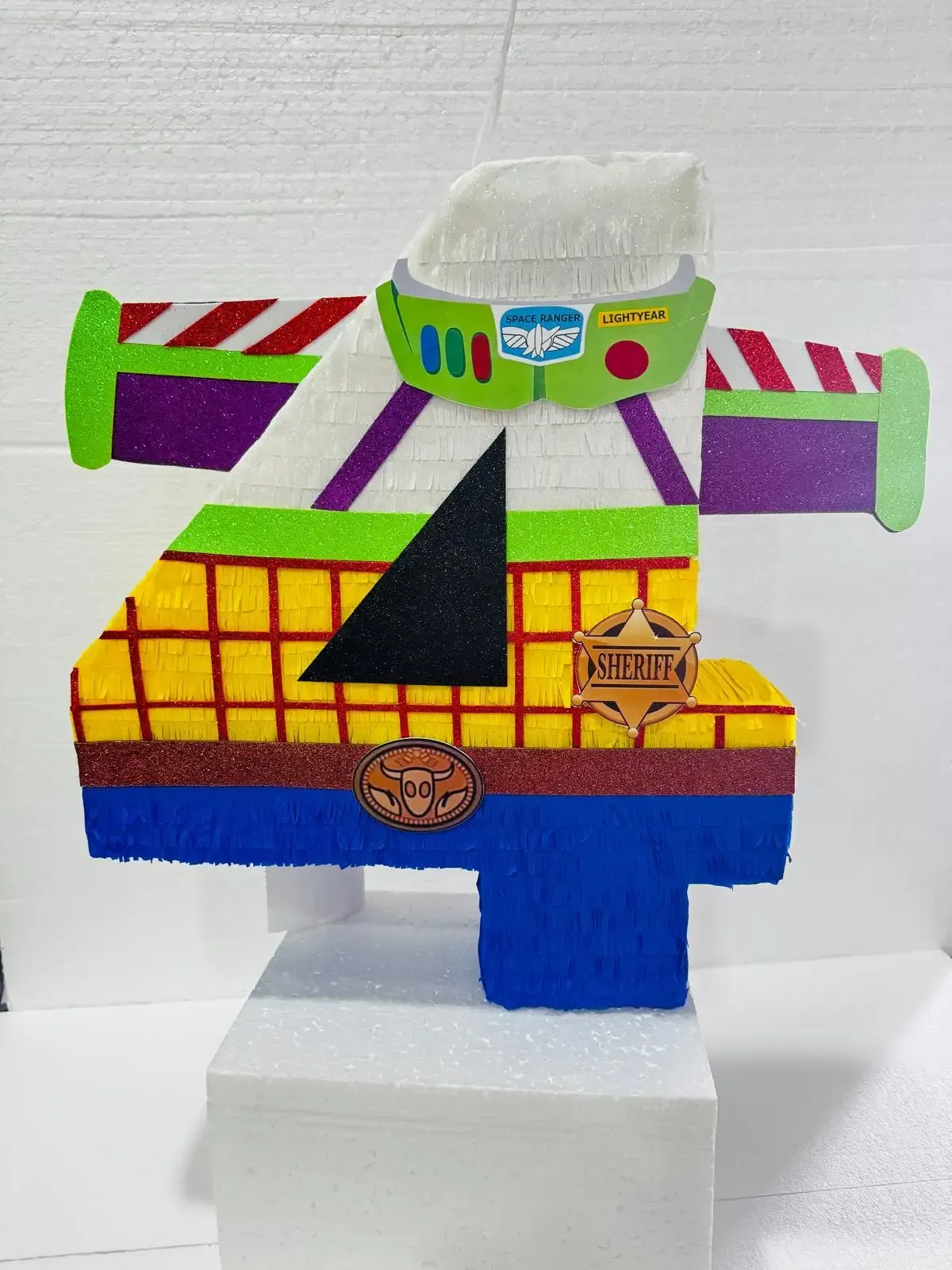 Avión de juguete casero y colorido, hecho de espuma, con secciones verdes, moradas, amarillas y azules sobre una base blanca.