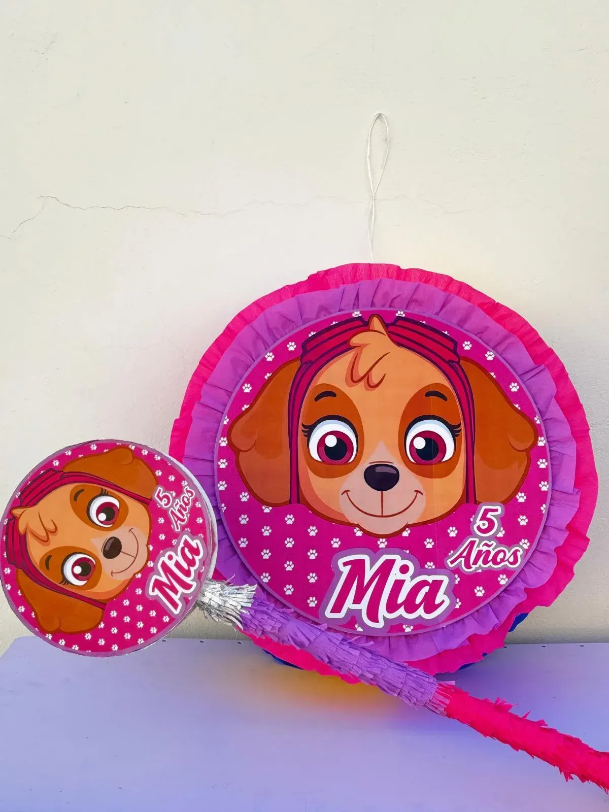 Globo circular rosa de Paw Patrol con la imagen de Skye, además de un globo más pequeño a juego, sobre una pared blanca.