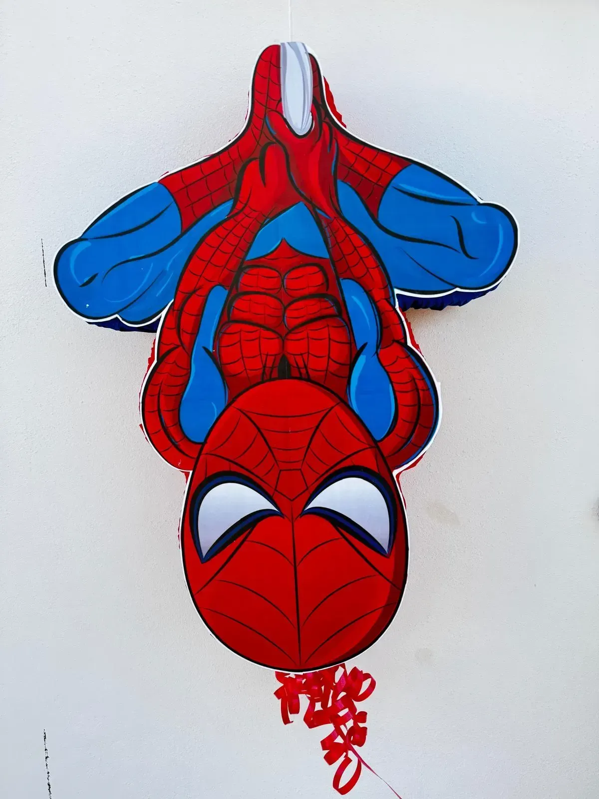 Spider-Man colgando boca abajo sobre un fondo blanco, en colores rojo y azul.