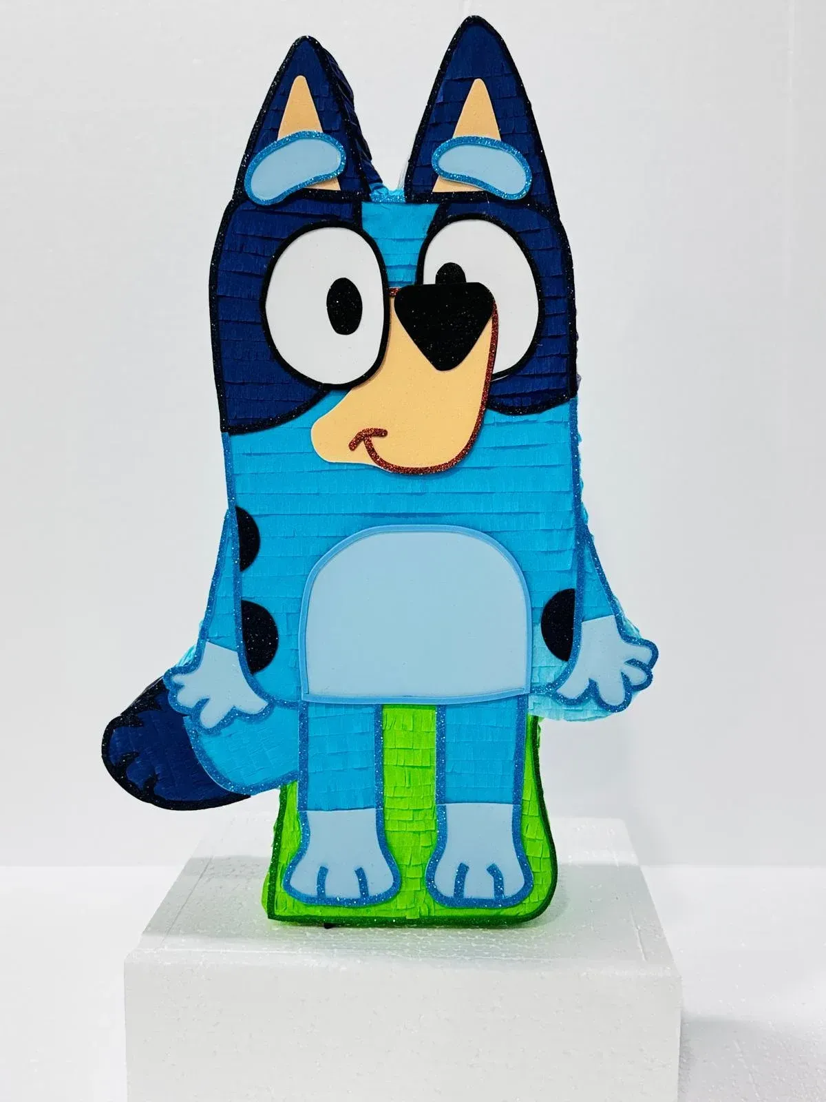 Figura de perro azul de dibujos animados con ojos grandes, de pie sobre un pedestal blanco sobre un fondo liso.