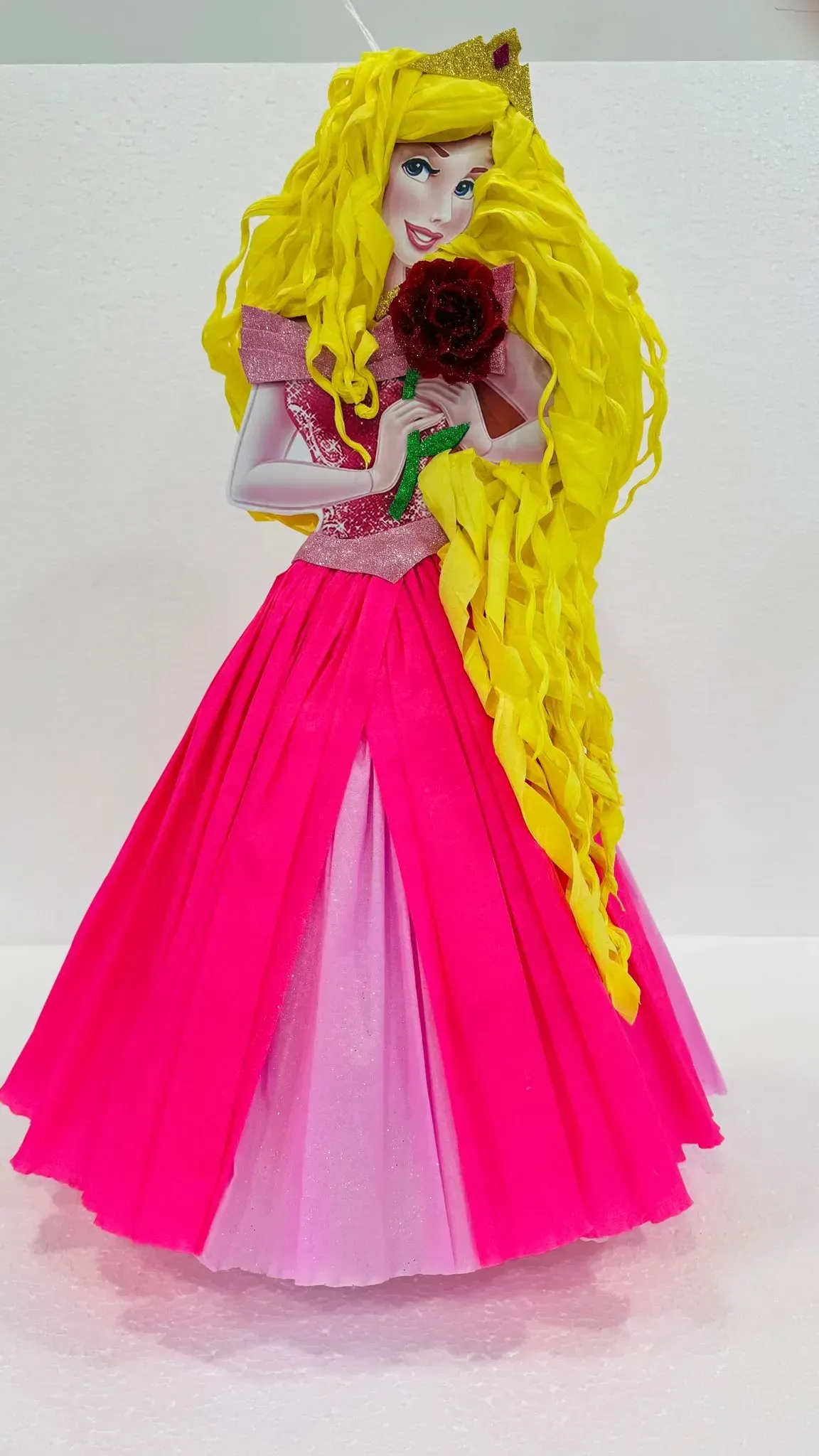 Muñeca llamativa con un vestido rosa fucsia y cabello largo y amarillo que sostiene un ramo de flores de color rojo oscuro.