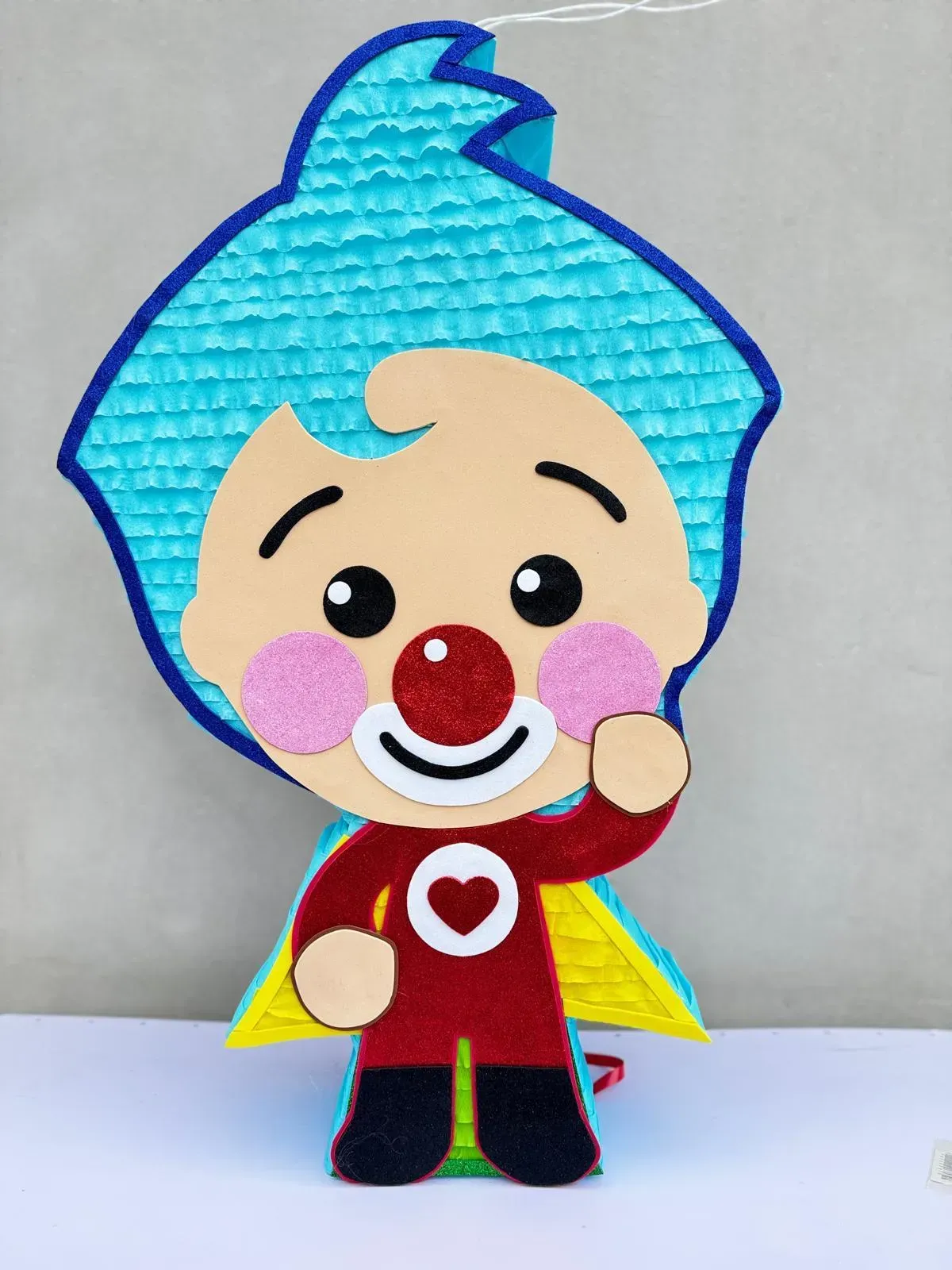 Payaso de dibujos animados con pelo azul, nariz roja y camiseta con un corazón sobre un fondo liso.