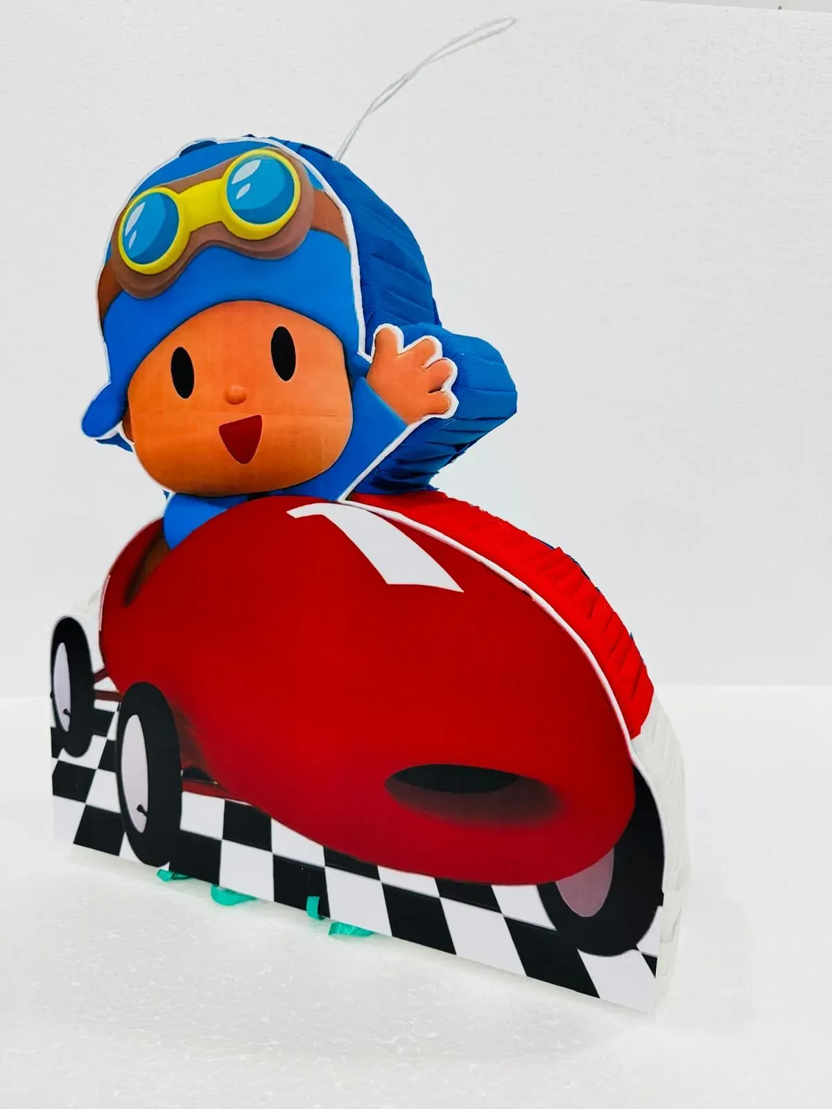 Un jinete de juguete con casco azul saluda desde un coche de carreras rojo de dibujos animados sobre una base de pista a cuadros.