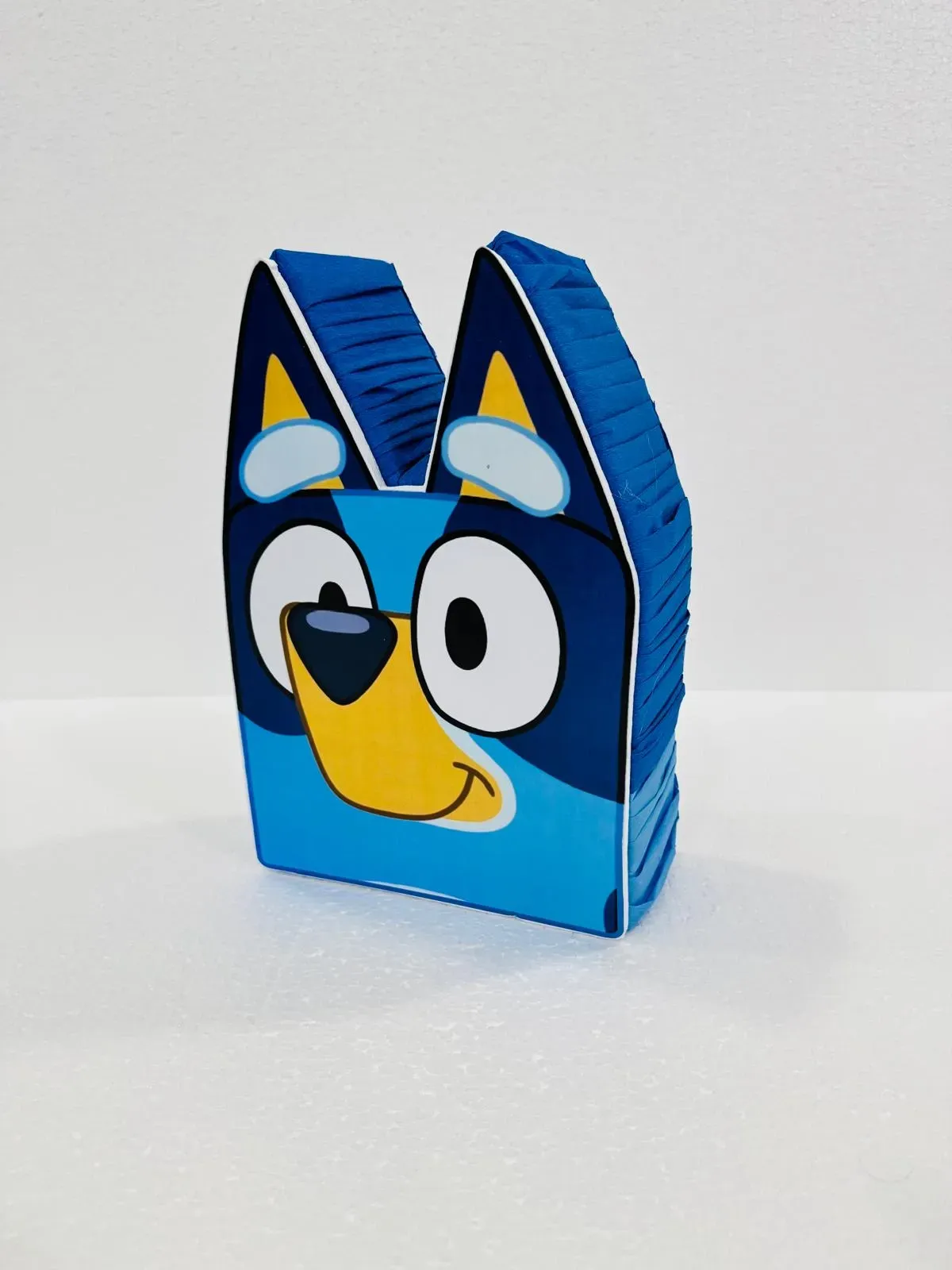 Figura de papel azul con forma de perro de dibujos animados con una cara sonriente sobre fondo blanco.