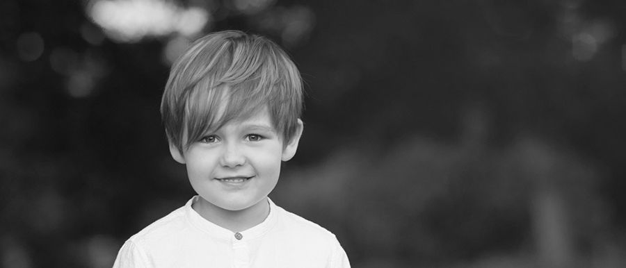 Auf einem Schwarzweißfoto lächelt ein kleiner Junge im weißen Hemd.