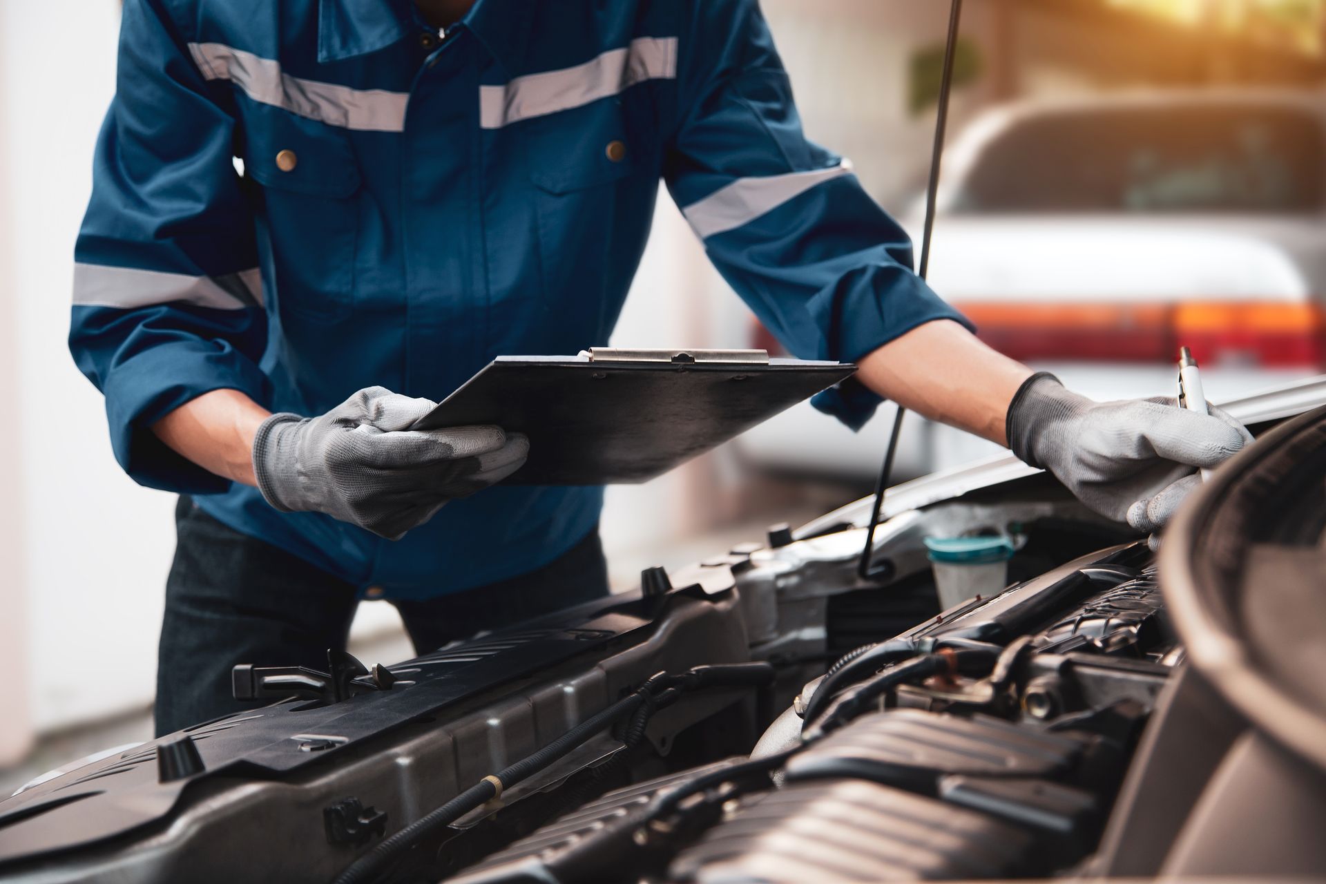Un mécanicien en uniforme bleu inspecte le moteur d'une voiture.