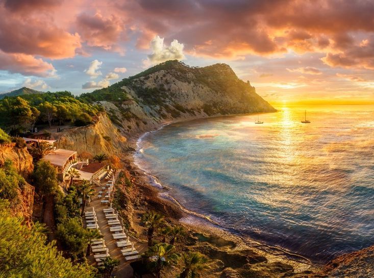 Una vista de una playa al atardecer con una montaña al fondo.